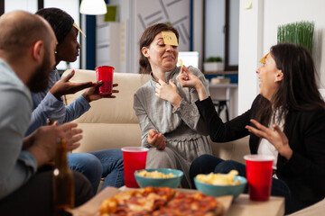 Diverse group of coworkers playing guess who game with sticky notes on forehead, enjoying fun activity with charades play. People guessing pantomime at drinks celebration after work hours.