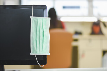 Face mask hanging on the computer screen in an empty office