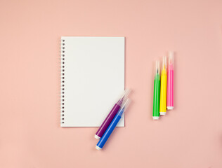 Blank notebook with colorful markers on a pink background with copy space. Business and education concept.