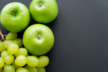top view of tasty apples and green grapes on black.