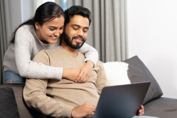 Cheerful couple in love spending leisure time online with a laptop at home. Young woman and man...