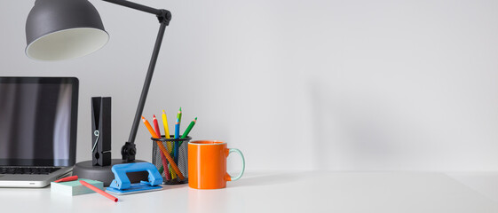 Creative desk with blank picture frame space or poster, desk objects, office supplies, books and plant on a gray background. Banner.