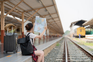Young asian woman using generic local map, siting alone at train station platform with luggage....