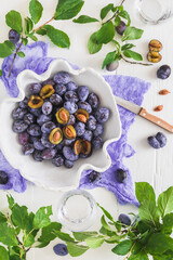 White handmade bowl filled with ripe plums, some of them sliced