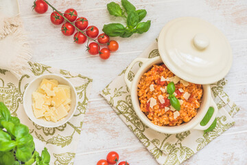 Homemade tomato risotto with fresh basil and parmesan cheese on a white wooden table