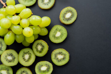 Naklejka na ściany i meble top view of green ripe grapes and sliced kiwi on black.