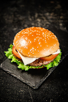 A burger on a stone board on a table. On a black background. High quality photo