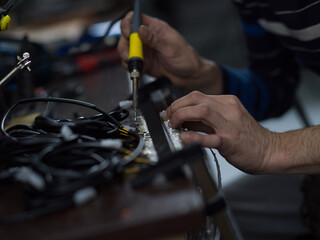 Fototapeta na wymiar Industrial worker man soldering cables of manufacturing equipment in a factory. Selective focus