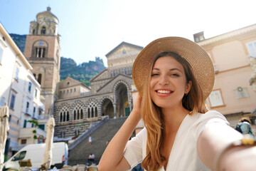 Happy young beautiful tourist girl taking a selfie smiling at the camera in the town of Amalfi,...