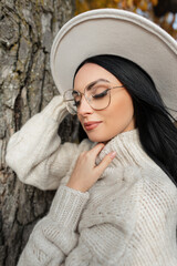 Autumn portrait of a beautiful stylish woman with vintage eyewear, hat and knitted sweater in an autumn park near a tree