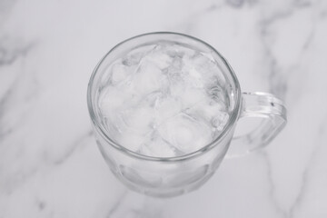 drinking enough water or sobriety concept, pint glass with tap water and ice cubes over marble background