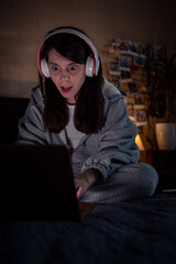 woman with wonder face sitting on the bed looking at laptop screen