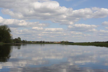 Picturesque and peaceful cloudscape with white clouds and blue sky reflecting in the river in spring or summer in Poland