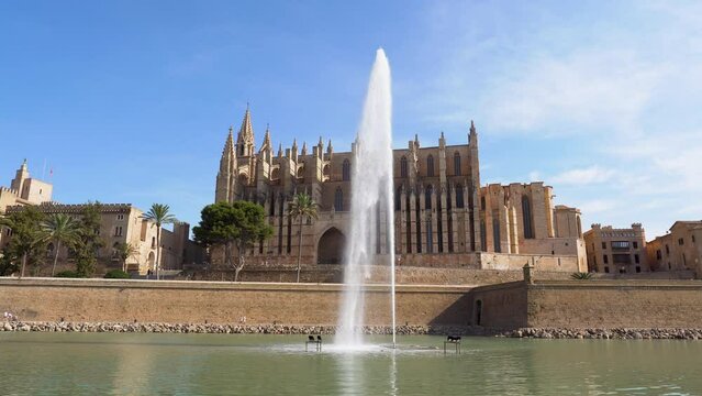 Pan over Cathedral (La Seu) and Royal Palace (Almudaina) in Palma de Mallorca with pond and fountain in the foreground - Spain