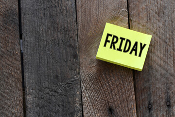 The word FRIDAY on a small piece of paper laid on a wooden table.