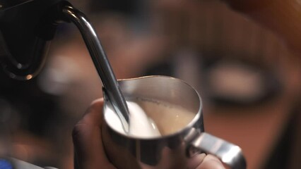 Process of preparing milk foam for cappuccino or latte, heating and whipping. Barista steaming milk in the pitcher. slow motion.