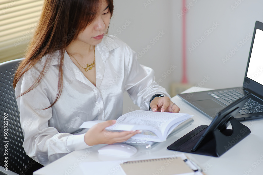 Poster Businesswoman working on laptop computer and reading a business book