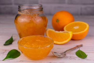 Orange jam in a glass jar on a white wooden background.