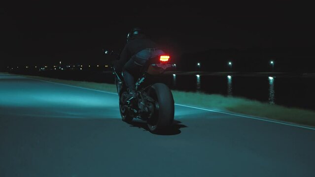 A man rides a sports motorcycle through the city at night against the backdrop of the river