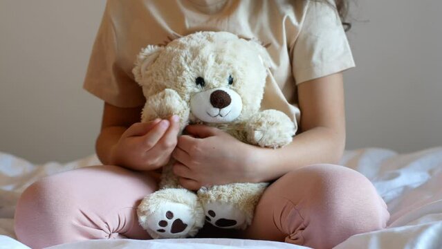 Child hugs and cuddles a cute beige teddy bear
