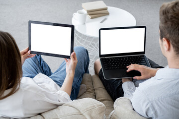 Digital life. Family couple. Computer mockup. Unrecognizable man and woman sitting with laptop and tablet computer blank screen in light room interior.