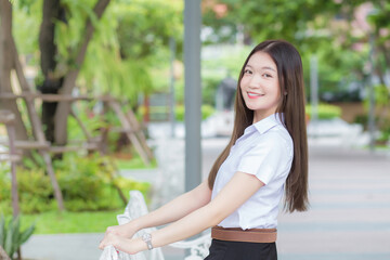 Portrait of an adult Thai student in university student uniform. Asian beautiful girl sitting smiling happily at university with a background of garden trees.