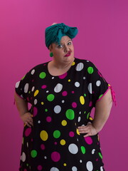 Plus size sexy model woman with trendy makeup, fashionable blonde in black short dress posing at the pink background in studio.
