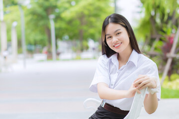 Portrait of adult Thai student in university student uniform. Asian beautiful girl sitting smiling happily at outdoors university with a background of outdoors garden trees.