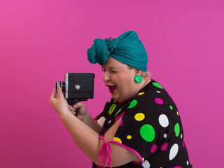 plus size smiling woman with funny emotional face expression with vintage camera in dress isolated on pink background, traveler on vacation, summer fashion style, excited tourist.