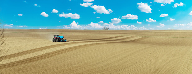 Farmer with tractor seeding crops at field. blue tractor with harrow in the field against a cloudy...