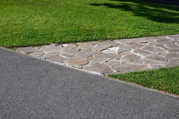 asphalt road near garden path made of natural stone paved with rough rock in a park with a green lawn, the decorative path with an abstract pattern.