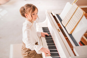 A little girl plays a big white piano in a bright sunny room © Maria Moroz