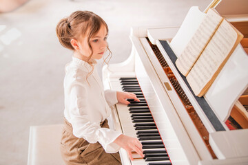 A little girl plays a big white piano in a bright sunny room