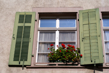 Facade of historic house at the old town of Basel with window, green wooden shutters and red flowers. Photo taken April 27th, 2022, Basel, Switzerland.