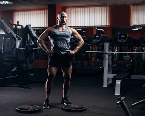 Fototapeta premium Serious sports man standing and posing in gym and looking aside.