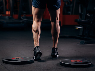 Trained legs with muscular calves in sneakers in fitness training gym