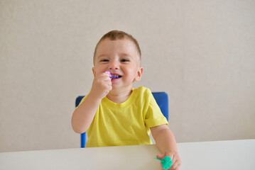 toddler boy plays constructor while sitting at a white table. educational game Montessori fine motor skills. early development concept. takes dangerous toys in his mouth