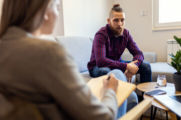 Young man talking to female psychologist during session. - obrazy, fototapety, plakaty