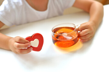 A girl in a white T-shirt holds a cup of tea and a liver in the form of a red heart. delicious sweet snack concept.