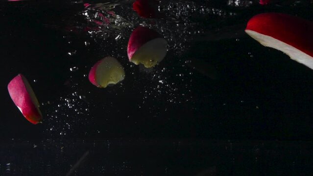 Slow motion underwater shot of delicious red apples falling into the water and spreading out, then floating back up, close up, cut out
