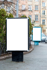 Two vertical billboards on the sidewalk, one in the foreground, the other behind the first in the background.