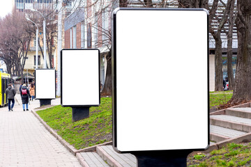 Three vertical billboards on the sidewalk, one in the foreground, the other behind the first in the...