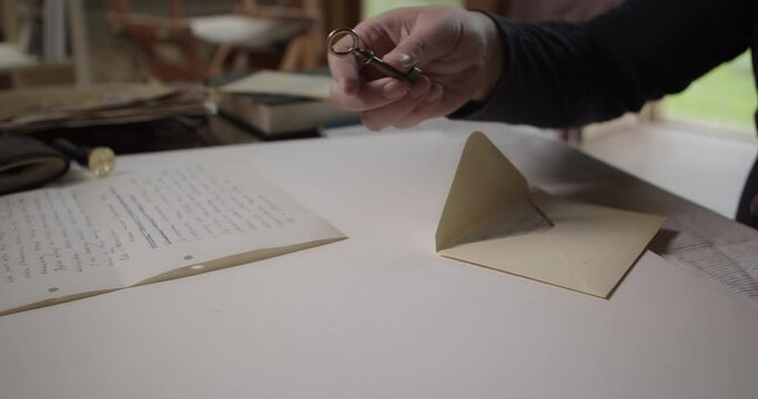 A man's hand takes a small key from the table and puts it in an envelope