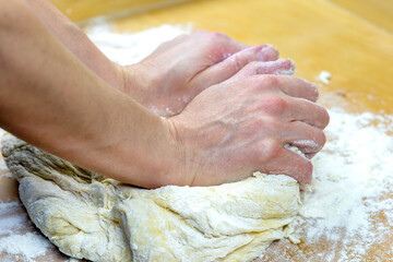 Female hands knead the dough on the table.