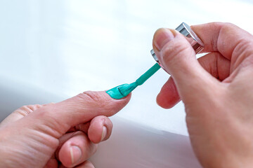 A woman applies a nail polish to her thumb nail with a brush.
