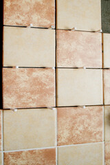 A section of freshly laid brown and cream tiles on the wall with plastic gaskets. Repair work