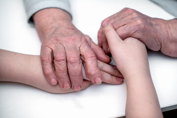 The grandson's hands hold the wrinkled hand of a sick elderly grandmother in a medical clinic. The...