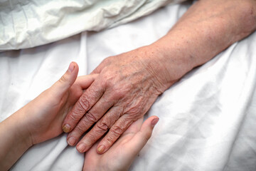 The grandson's hands hold the wrinkled hand of a sick elderly grandmother in a medical clinic. The concept of love and care. Slow movement