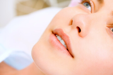 Image of a young beautiful woman dressed as a patient, lying on a couch in a cosmetology clinic.