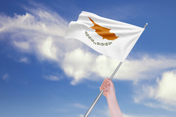 Female Hand is Waving Cyprus Flag Against Blue Sky with Clouds